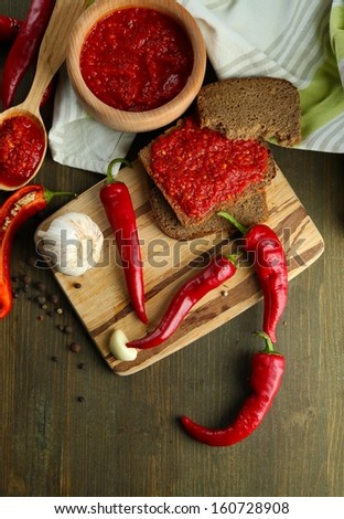 Composition with salsa sauce on bread,, red hot chili peppers  and garlic, on napkin,  on wooden background