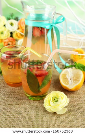 Basil lemonade with strawberry in  jug and glass, on wooden table, on bright background