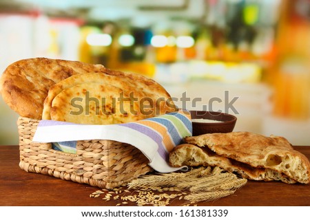 Pita breads in basket with spikes and flour on table on bright background