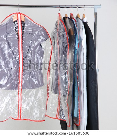Office female clothes in cases for storing on hangers, on gray background