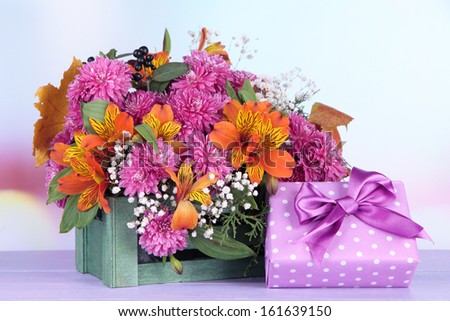 Flowers composition in crate with present on table on bright background