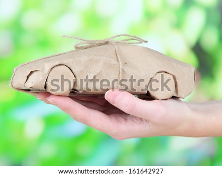 Woman hand holding a car wrapped in brown kraft paper, on nature background