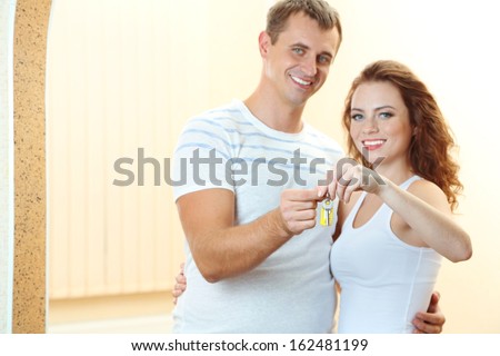 Young couple with keys to your new home on room background