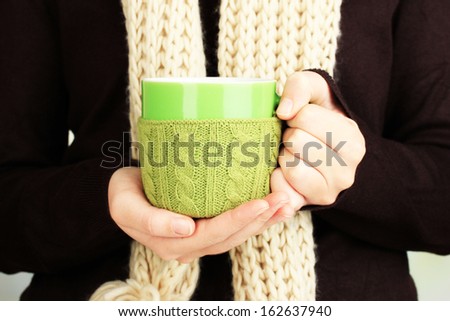 Cup with knitted thing on it in female hands close up
