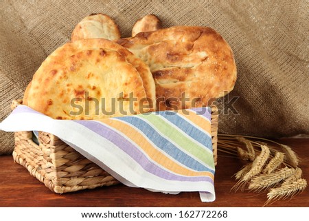 Pita breads in basket with spikes on table on sackcloth background
