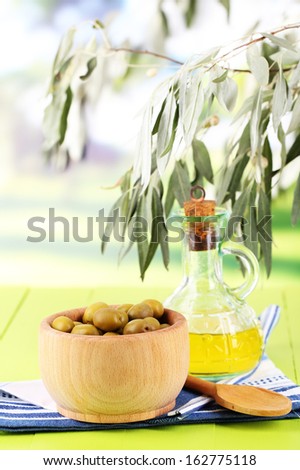 Olive oil and olives in bowl on napkin on wooden table on nature background