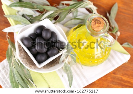 Olives in bowl and oil with branch on napkin on wooden board on table