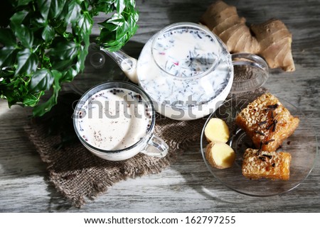 Teapot and cup of tea with milk and spices on sackcloth of wooden table