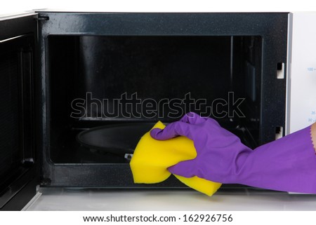 Hand with sponge cleaning  microwave oven, isolated on white