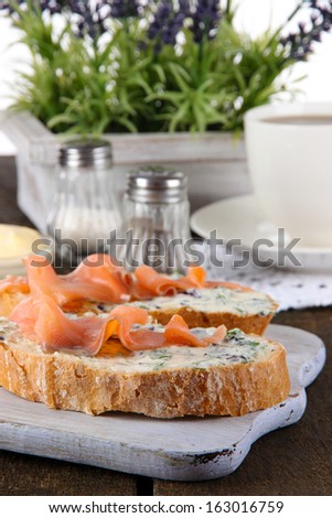 Fish sandwiches and cup of tea on cutting board on wooden table