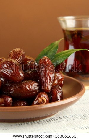 Dried dates on plate with cup of tea on table on brown background