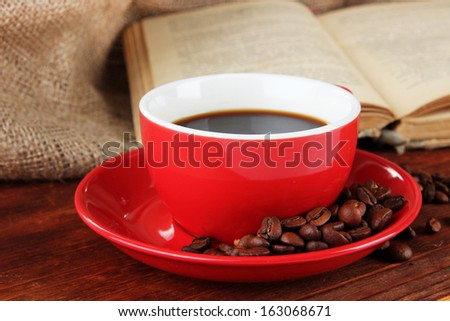 Cup of coffee with coffee beans and book on wooden table on sackcloth background
