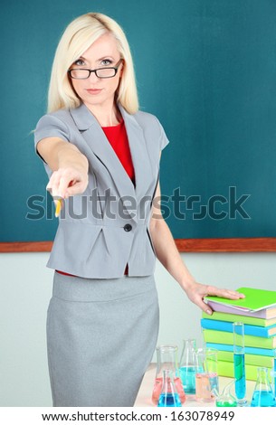 Chemistry teacher standing near table with tubes on blackboard background