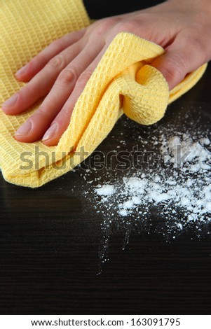 Hand wiping wooden surface with yellow rag