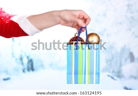 Hand holds package with New Year balls on snow background