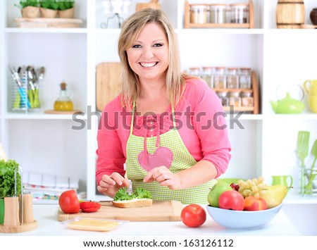 Happy smiling woman in kitchen preparing  sandwich