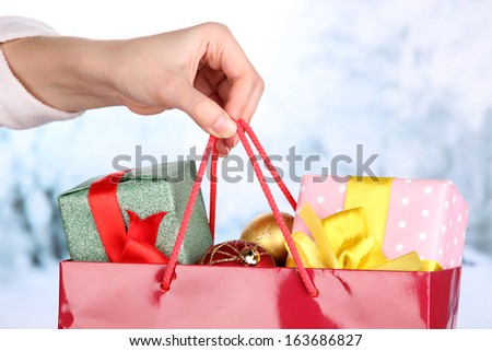 Hand holds package with New Year balls and gifts on snow background