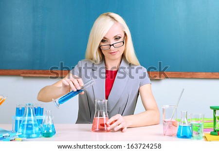 Chemistry teacher with tubes sitting at table on blackboard background