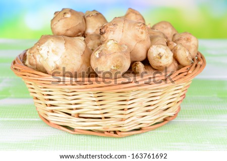 Topinambur roots in wicker basket on table on light background