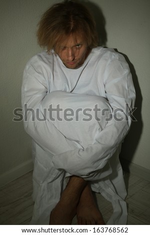 Mentally ill man in strait-jacket in room corner