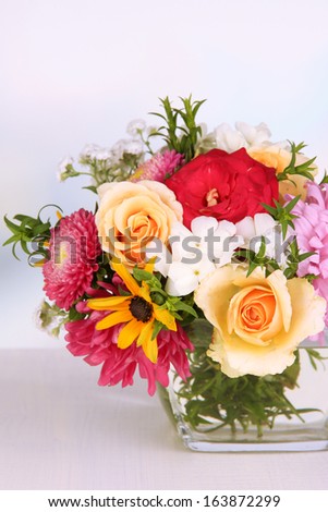 Beautiful bouquet of bright flowers in glass vase, on wooden table, on bright background