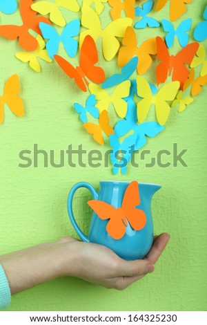 Paper butterflies fly out of pitcher on green wall background