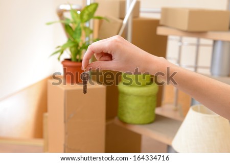 Female hand with keys ob stack of cartons background: moving house concept