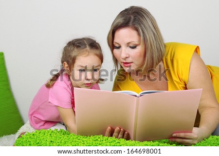 Little girl with mom read book in bed