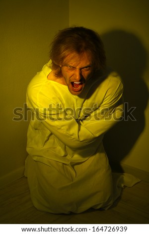 Mentally ill man in strait-jacket in room corner