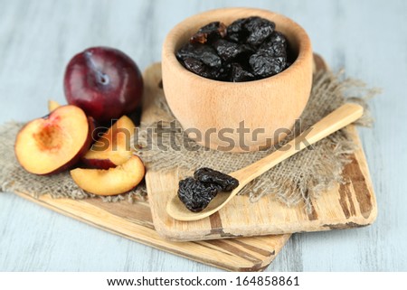 Fresh and dried plums in wooden bowl on napkin, on wooden background