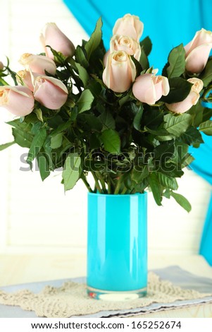Beautiful bouquet of roses in vase, on light wooden background