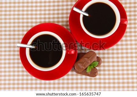 Red cups of strong coffee with chocolate bars on squared background