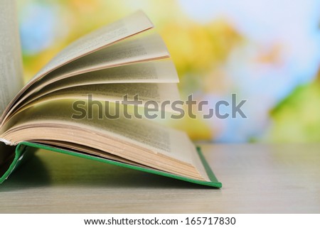Opened book on wooden table on natural background