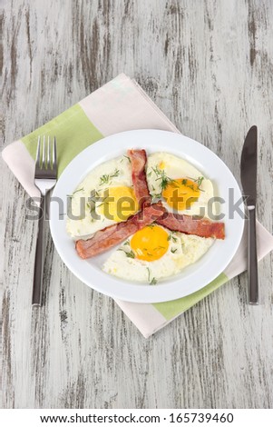 Scrambled eggs and bacon on plate on napkin on wooden table