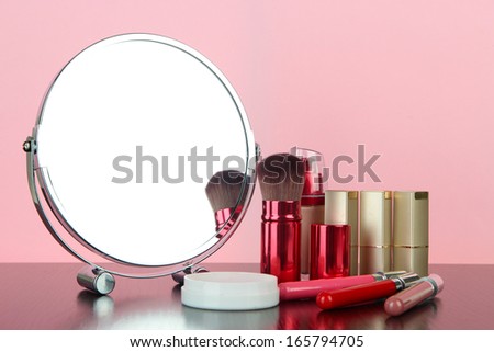 Round table mirror with cosmetics on table on pink background