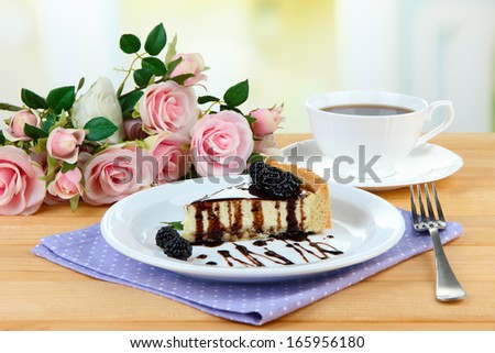 Slice of cheesecake with chocolate sauce and blackberry on plate, on wooden  table, on bright background