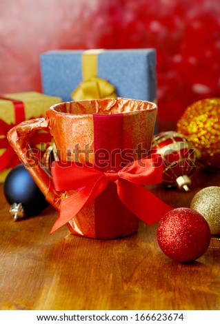 Cup packed in gift paper with gifts on wooden table on bright background