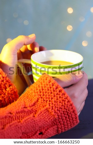 Hands holding mug of hot drink, close-up, on bright background