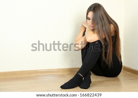 Lonely sad woman sitting on floor near wall