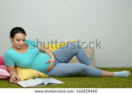 Young pregnant woman lying on floor and reading book on wall background