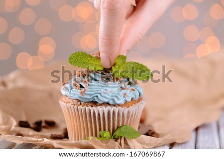 Female hand decorating tasty cupcake with butter cream, on color wooden table, on lights background