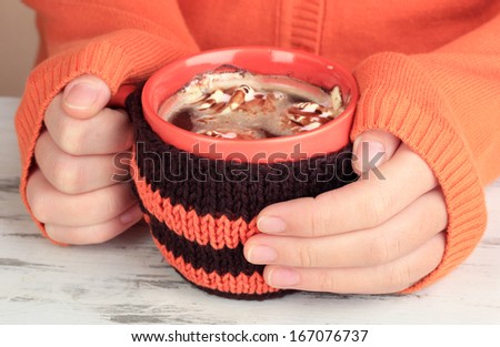 Cup with knitted thing on it in female hands close up