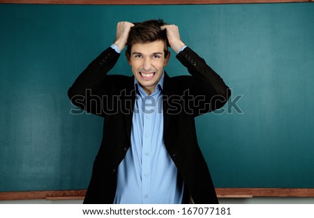 Young teacher near chalkboard in school classroom