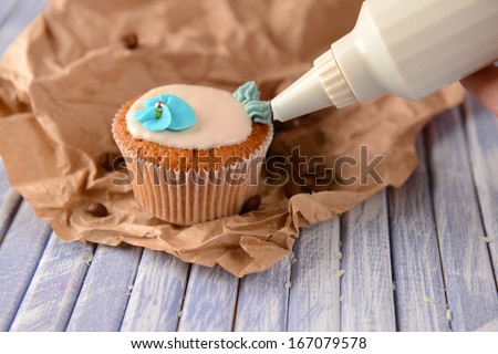 Confectioner decorating tasty cupcake with butter cream, on color wooden background