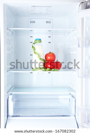 Conceptual photo of diet: apple and milk bottle with measuring type on shelf of refrigerator