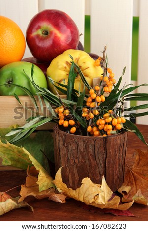 Different fruits in box and branch of sea buckthorn on table on fence background