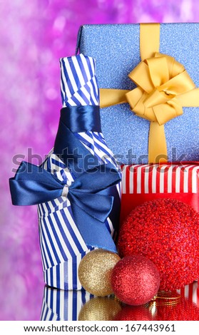 Bottle packed in gift paper  with gifts on purple background