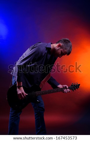 Young musician playing  guitar on dark color background