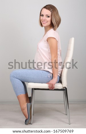 Young regnant woman sitting on chair on wall background