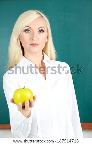 School teacher near blackboard with apple in classroom
